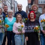 Gruppenfoto des neu gewählten Vorstands von BÜNDNIS 90/DIE GRÜNEN Rendsburg-Eckernförde in einer Innenstadt. Vorn von links nach rechts: Caroline Sindern, Ulrike Driller-Brunkhorst, Hanna Engel und Britta Mohr. Hinten von links nach rechts: Markus Suhr, Ingmar Jaschok-Hops, Dennis Stüber und Oliver Berndt. Alle halten Sonnenblumen in den Händen.
