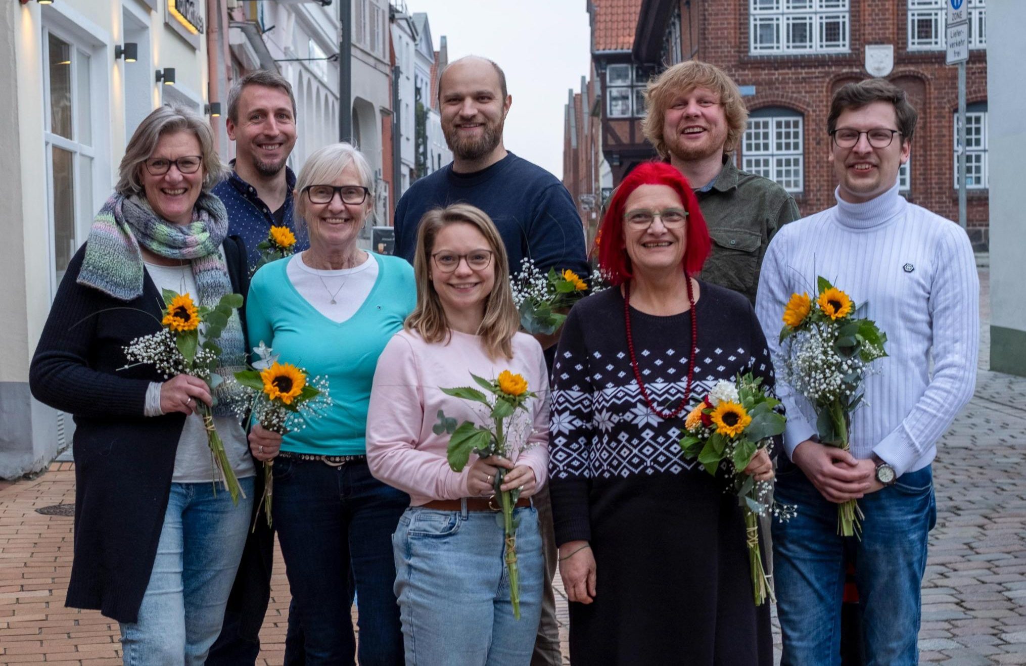Gruppenfoto des neu gewählten Vorstands von BÜNDNIS 90/DIE GRÜNEN Rendsburg-Eckernförde in einer Innenstadt. Vorn von links nach rechts: Caroline Sindern, Ulrike Driller-Brunkhorst, Hanna Engel und Britta Mohr. Hinten von links nach rechts: Markus Suhr, Ingmar Jaschok-Hops, Dennis Stüber und Oliver Berndt. Alle halten Sonnenblumen in den Händen.