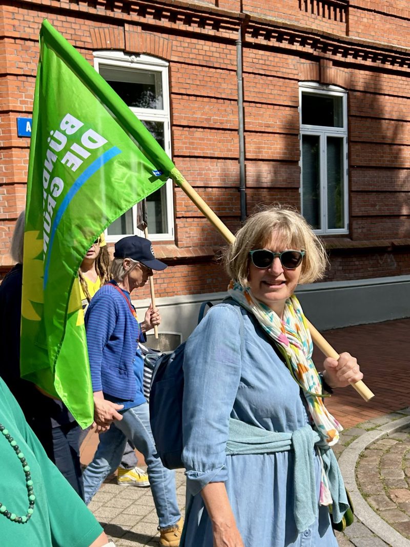 Meike aus dem Kreisvorstand trägt eine Fahne mit der Aufschrift "BÜNDNIS 90/DIE GRÜNEN", im Hintergrund sind weitere Demo-Teilnehmende zu sehen